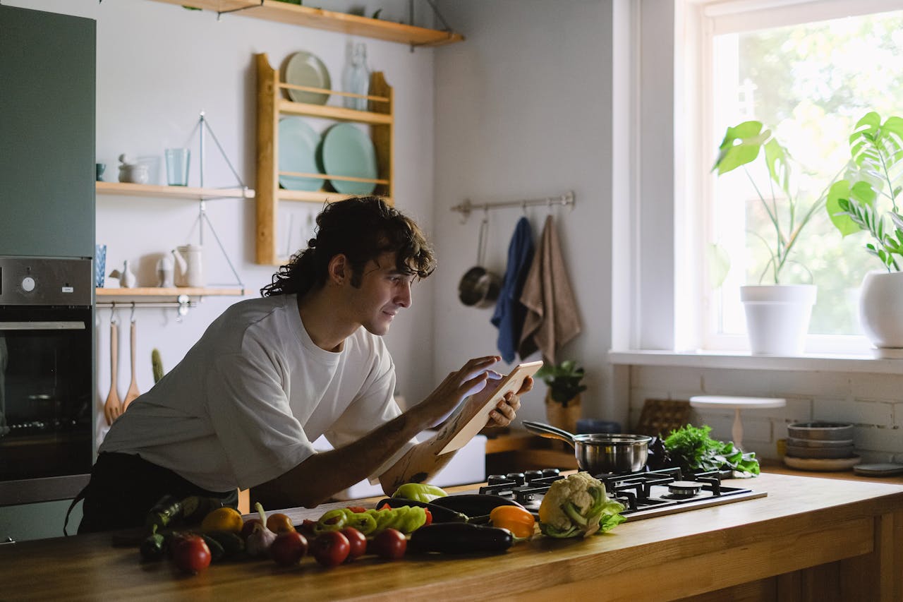 Man preparing food in the kitchen using a tablet for recipe guidance. Vibrant and modern setting.